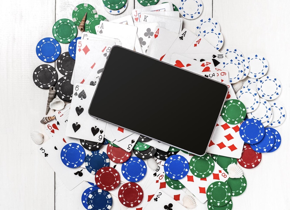 Tablet leżący na stole wśród żetonów do pokera i kart do gry